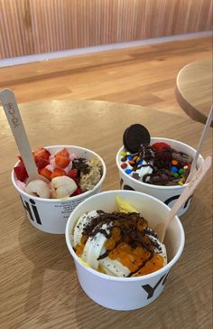 three ice cream bowls with different toppings in them sitting on a wooden table top