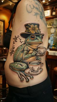 a frog wearing a top hat and holding a coffee cup tattoo on the side of a woman's stomach