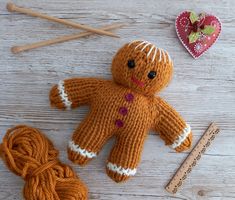 an orange knitted teddy bear next to yarn and knitting needles on a white wooden surface