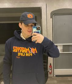 a young man taking a selfie with his cell phone wearing a hat and sweatshirt