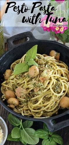 pesto pasta with tuna in a cast iron skillet on a wooden table surrounded by flowers and herbs