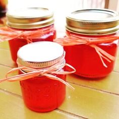 three jars filled with red liquid sitting on top of a wooden table next to each other