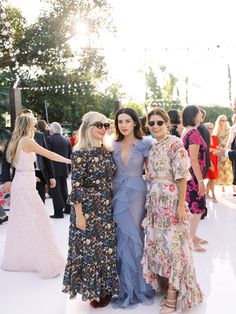 three women standing next to each other in front of a group of people wearing dresses