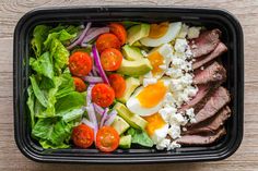 a salad with meat, tomatoes, lettuce and eggs in a black container