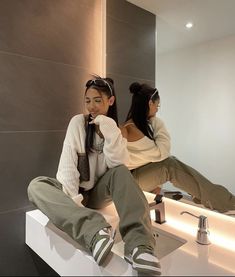 two young women sitting on a counter in front of a mirror, one brushing her teeth