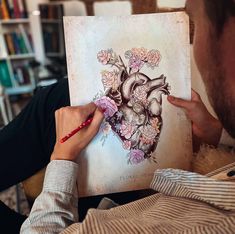 a man is holding up a book with a heart drawn on it and flowers in the middle