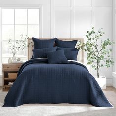 a bed with blue comforters and pillows in a white room next to a window