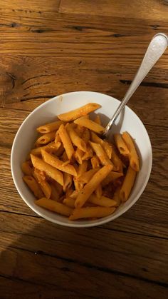 a white bowl filled with french fries on top of a wooden table next to a spoon