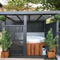 an outdoor hot tub surrounded by potted plants and wooden planters in front of a black fence