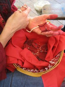 a woman sitting on the ground holding something in her hand and wearing red shirt with gold trim