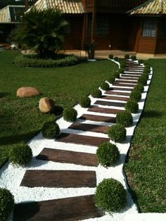 a garden path made out of wood and white gravel in front of a house with grass