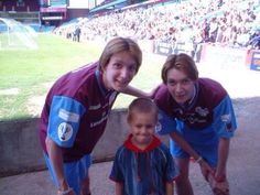 three young children standing next to each other in front of a crowd at a soccer game