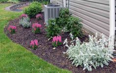 a flower bed in front of a house next to a air conditioner and flowers