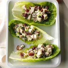 three lettuce wraps with chicken and cranberry salad on them sitting on a white plate