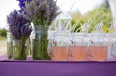 lavender flowers are in mason jars on a purple table cloth with drinking glasses and straws