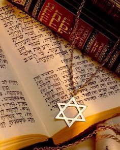 an open book with a silver star of david on it next to a chain necklace