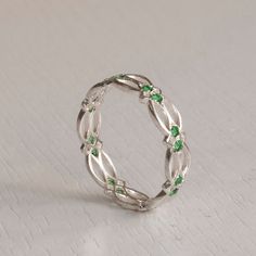 a silver ring with green stones on the inside is sitting on a white tablecloth