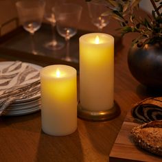 two lit candles sitting on top of a wooden table next to bread and wine glasses