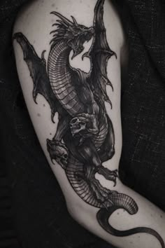 a black and white photo of a dragon tattoo on the right arm, with its wings spread