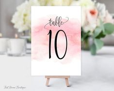 a table number sign sitting on top of a wooden easel with flowers in the background