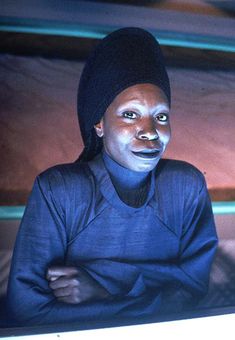 a woman with painted face sitting in front of a computer screen and looking at the camera