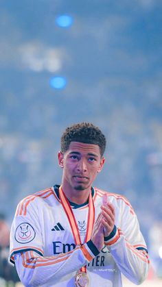 a man holding a silver medal in his right hand and wearing a white shirt with an orange ribbon around his neck