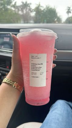 a person holding up a pink drink in their hand while sitting in the driver's seat