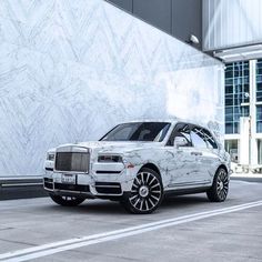 a white rolls royce parked in front of a building with graffiti on the side and black rims