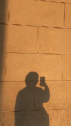 a shadow of a man holding a cell phone up to his face while standing in front of a brick wall