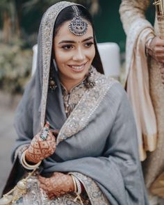 a woman wearing a gray and silver outfit with jewelry on her head, sitting down