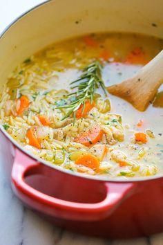 a red pot filled with chicken noodle soup next to a wooden spoon on a white counter