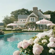 a large house sitting next to a pool with flowers in the foreground and an umbrella over it