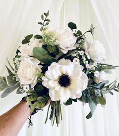 a bouquet of white flowers and greenery is held by a person's hand