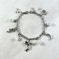 This "Clara Bow" themed charm bracelet is the perfect accessory to showcase your love for your favorite music in a subtle way. Charms included: Sparkling Stars Rose Bow Moon Crown 5 white selenite beads Comes in three sizes: Small: 6.5 inches (with extra rings at the end to expand up to 7.5 inches.) Standard: 7.5 inches Large: 8.5 inches Secures with a lobster clasp. Chain is stainless steel. Charms are made with zinc alloy. Beads are natural gemstones. All materials are lead and nickel free.  C Silver Beaded Bracelets With Moon Charm As Gift, White Dangle Charm Bracelet, White Metal Dangle Charm Bracelet, White Metal Charm Bracelet As A Gift, White Metal Charm Bracelet As Gift, White Dangle Charm Bracelet With Lobster Clasp, Metal Charm Bracelet With Moon Charm As A Gift, Music Inspired Jewelry, Clara Bow