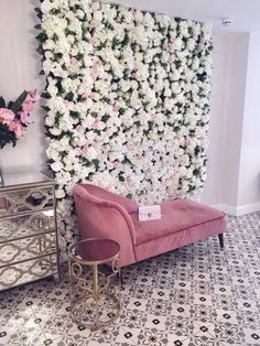 a pink couch sitting in front of a wall covered with white flowers next to a mirror