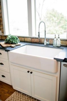 a white kitchen sink sitting under a window next to a counter top with a cutting board on it