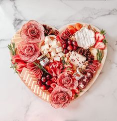 a heart shaped platter filled with meats, cheeses and flowers on a marble table