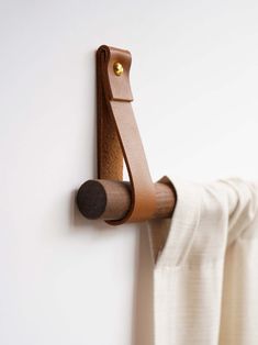 a wooden hook on the side of a white wall next to a curtain with a brown leather handle