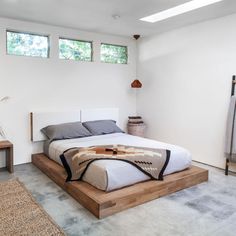 a bedroom with a bed, rugs and windows in the room that has white walls