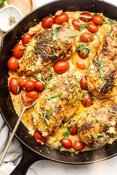 a skillet filled with chicken, tomatoes and cheese on top of a white table