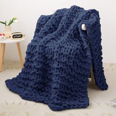 a blue knitted blanket sitting on top of a wooden chair next to a table