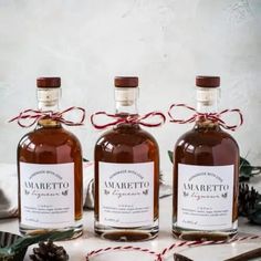 three bottles of marretto sit on a table with pine cones and twine