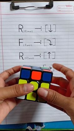 someone holding a rubik cube in front of a piece of paper with writing on it