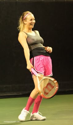 a woman holding a tennis racquet on top of a tennis court in front of a black wall