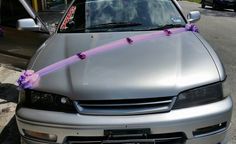 a silver car with purple ribbons tied to it's hood and the front window