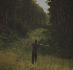 a man standing in the middle of a forest holding his arms out to the side