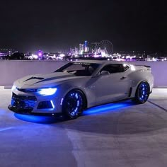 a white sports car with blue lights on it's hood parked in front of a cityscape