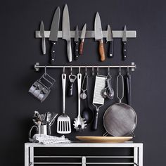 there are many knives hanging on the wall next to a rack with cooking utensils