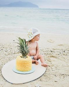 a baby sitting on the beach next to a pineapple cake