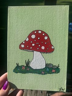 a hand holding up a small painting of a mushroom